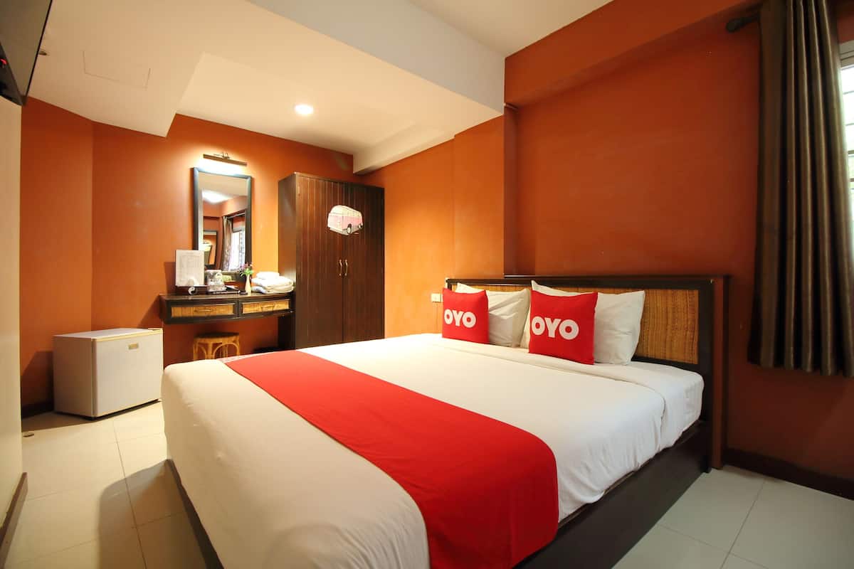 Hotelkamer met een groot bed, een kledingkast, een bureau met stoel en een kleine koelkast.