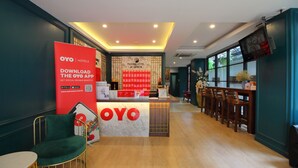Zona de recepción de hotel con mostrador, un anuncio rojo de la aplicación OYO y una zona de bar con sillas de madera.