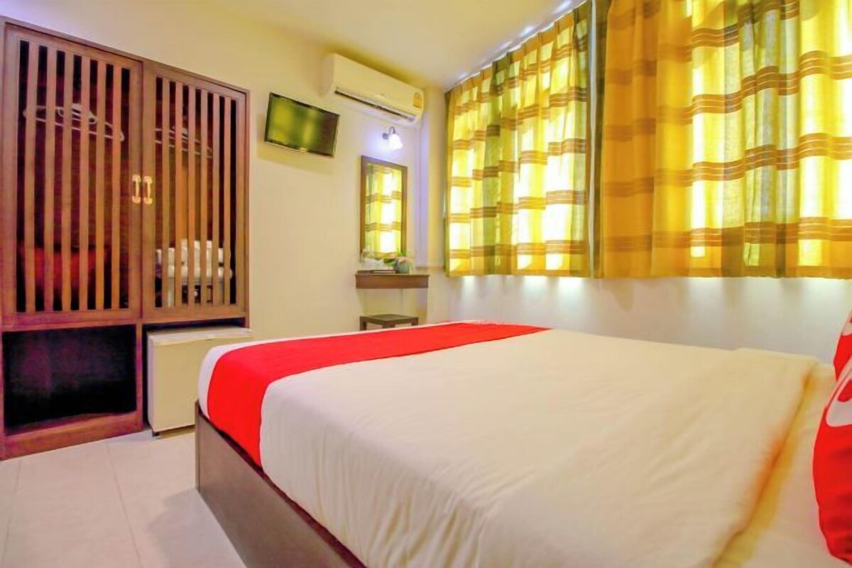 Una habitación de hotel con cama, armario, televisión y ventana con cortinas.