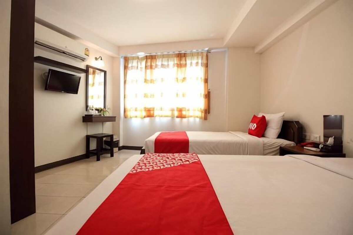 Habitación de hotel con dos camas, televisión, escritorio y ventana con cortinas.