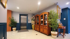 Un vestíbulo con mostrador de recepción, un mueble de madera, una planta en maceta y un ascensor.
