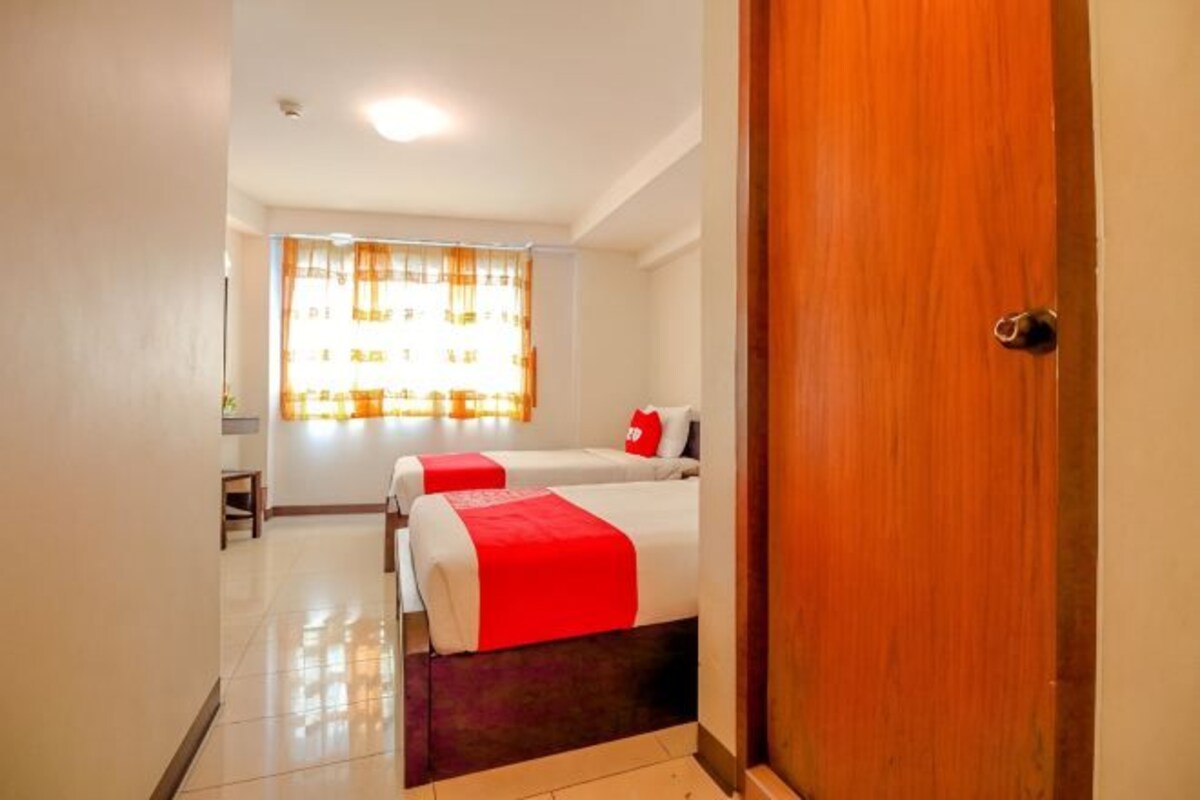 Habitación de hotel con dos camas, una puerta de madera y un ventanal con cortinas.