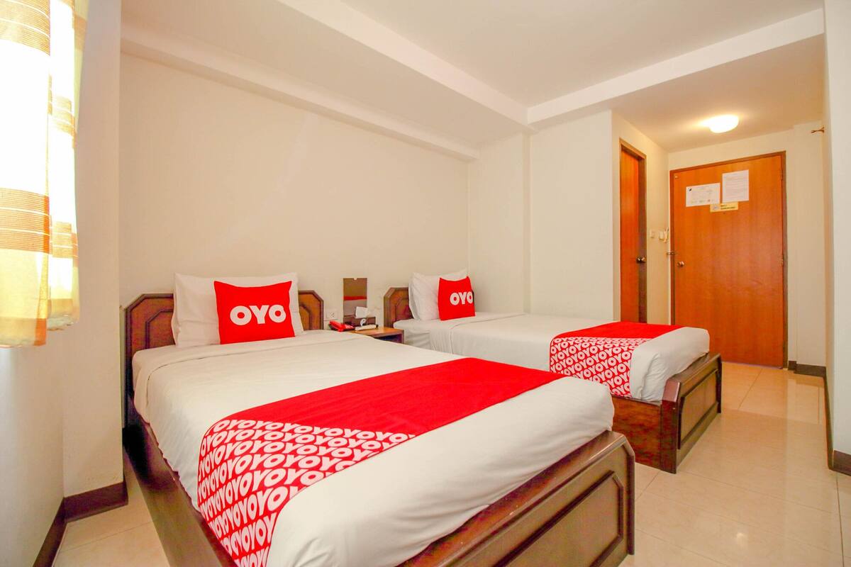 A hotel room with two beds, each with a red and white bedspread and pillows with the word "OYO" on them.