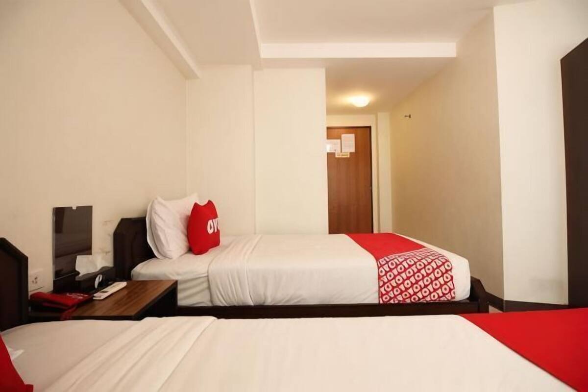 A hotel room with two beds, a desk, a chair, a TV, and a door leading to another room.