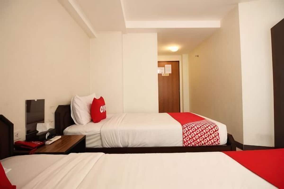 Quarto de hotel com duas camas, uma escrivaninha, uma cadeira, uma TV e uma porta que dá para outro cômodo.