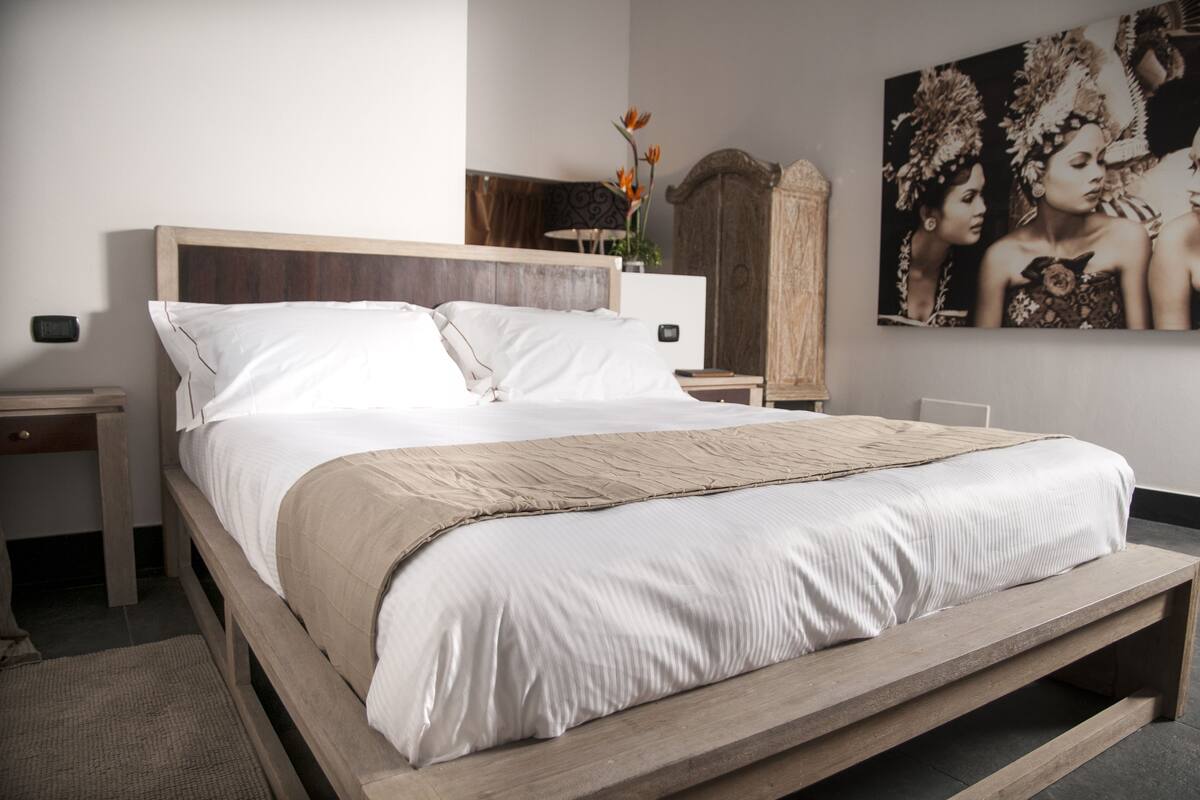 A neatly made bed with a wooden frame and white bedding, a nightstand with a lamp, and a wall-mounted artwork.
