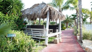 A thatched-roof gazebo with a bench, surrounded by lush greenery and palm trees. - Sevenmaze Charming House (Bari)