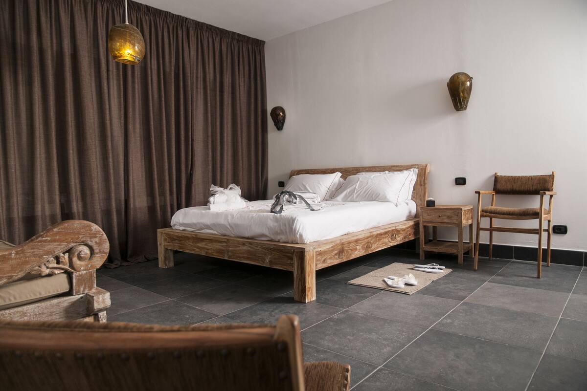 A bedroom with a wooden bed, a nightstand, a chair, and a large window with curtains.