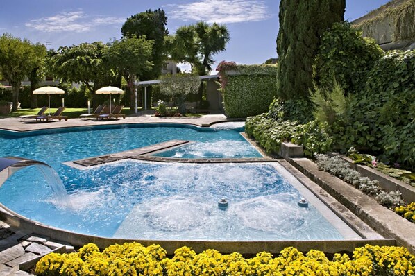 Una piscina con hidromasaje, rodeada de exuberante follaje y flores amarillas.