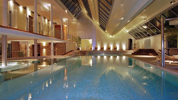 An indoor swimming pool with clear water, surrounded by a modern architectural design with glass railings and a staircase leading to an upper level. - Europa Terme (Abano Terme)