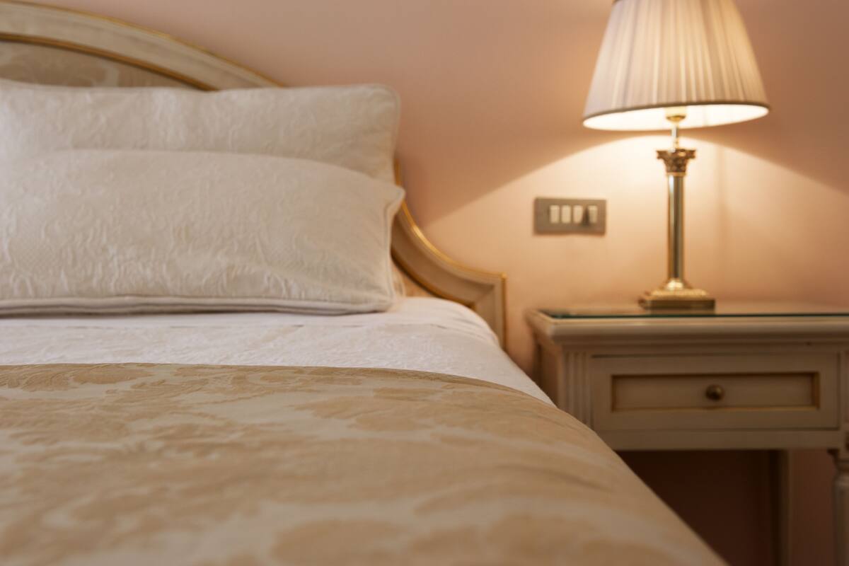 Una cama bien tendida con cabecera, una lámpara de noche y una mesita de noche con cajón.