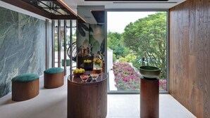A modern interior with a wooden bench, a round table with fruits, and a view of a garden through large windows. - Europa Terme (Abano Terme)