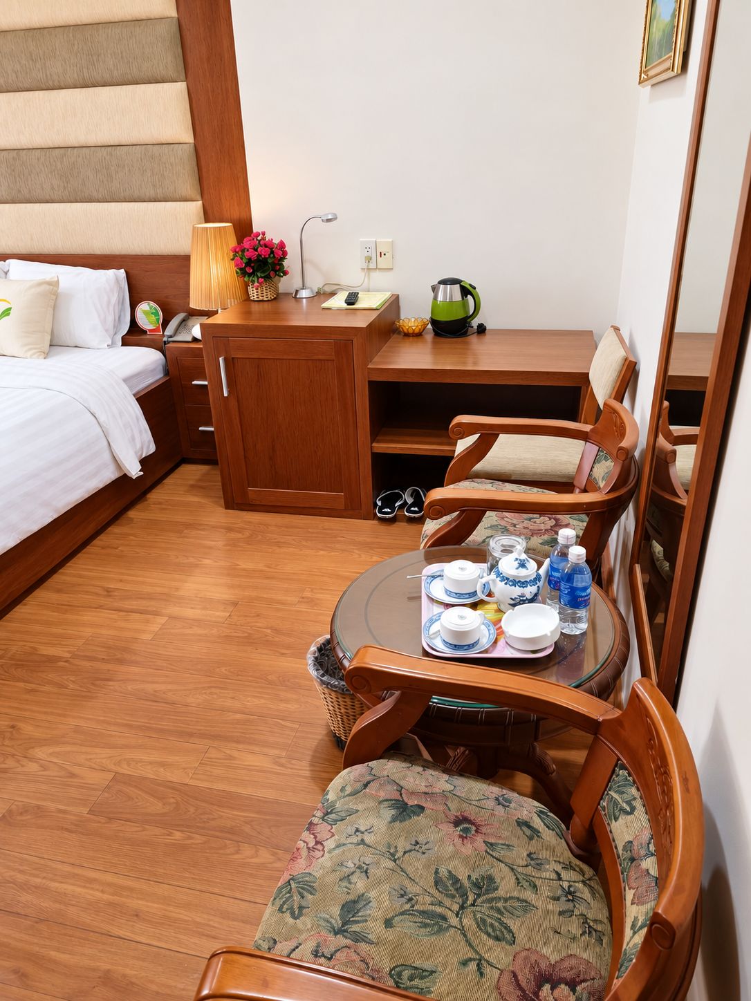 A hotel room with a bed, a wooden desk, a table with tea set, and chairs.