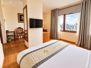 A hotel room with a bed, a desk, a chair, a television, and a window with a city view. - Moonlight Da Nang Hotel (Da Nang)
