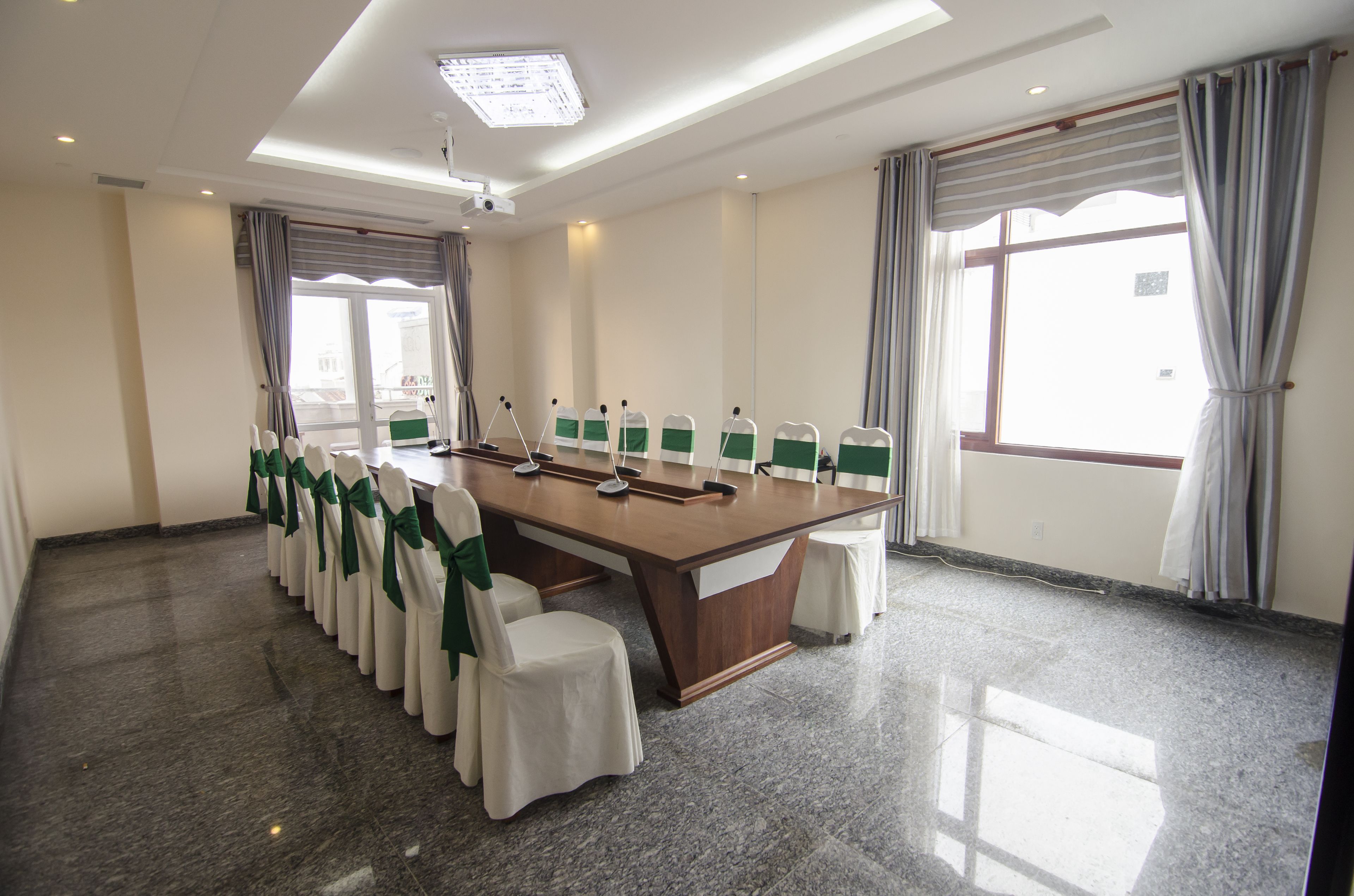 A conference room with a long table, chairs with green sashes, and large windows with curtains.
