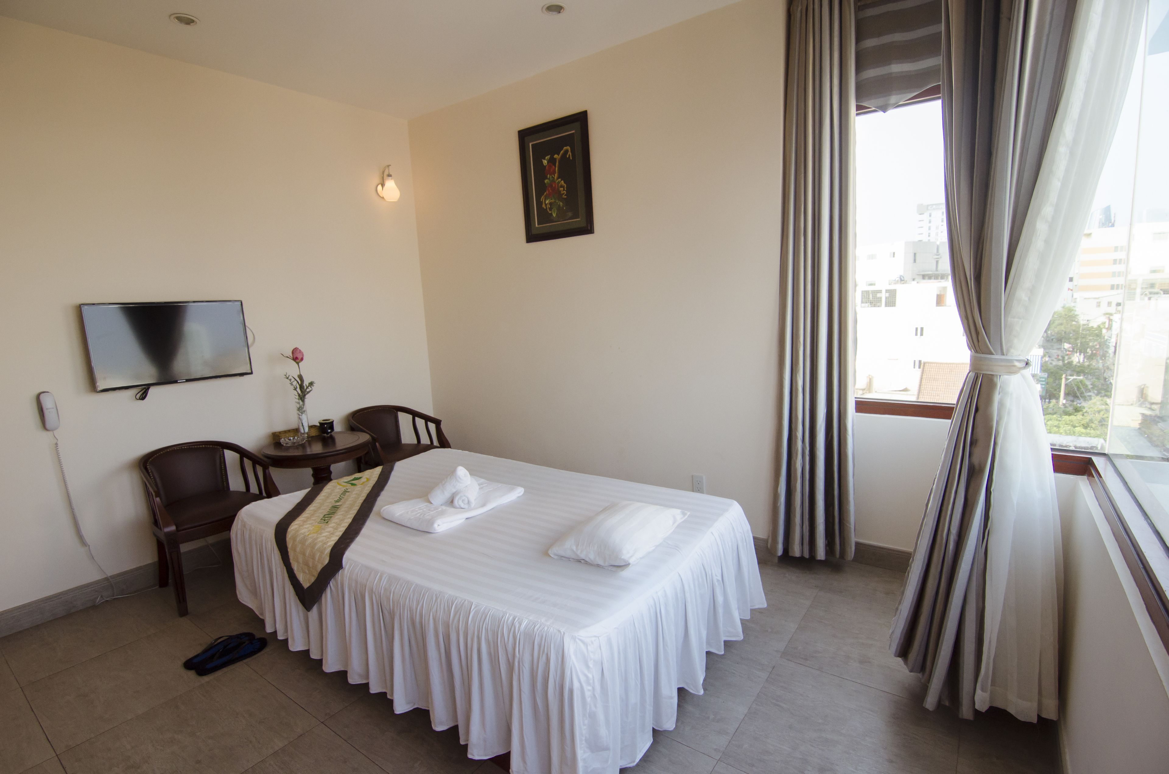 Habitación de hotel con cama, una silla, una mesita, televisor y ventana con cortinas.