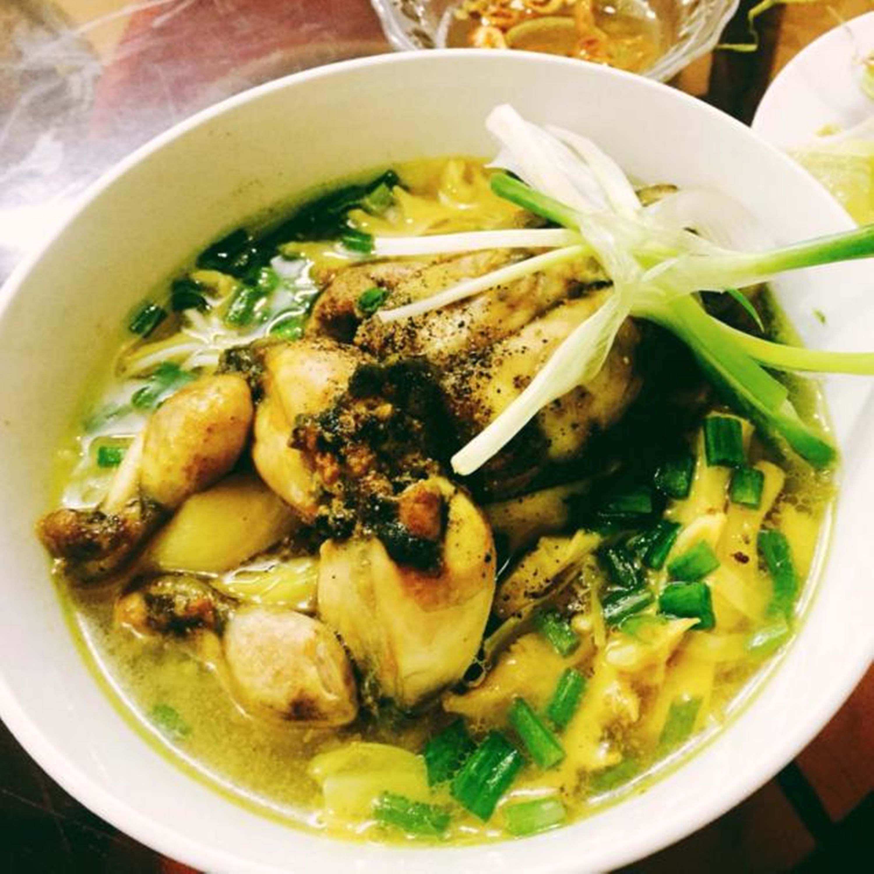 Eine Schüssel Suppe mit Hühnchen, Gemüse und Garnituren.