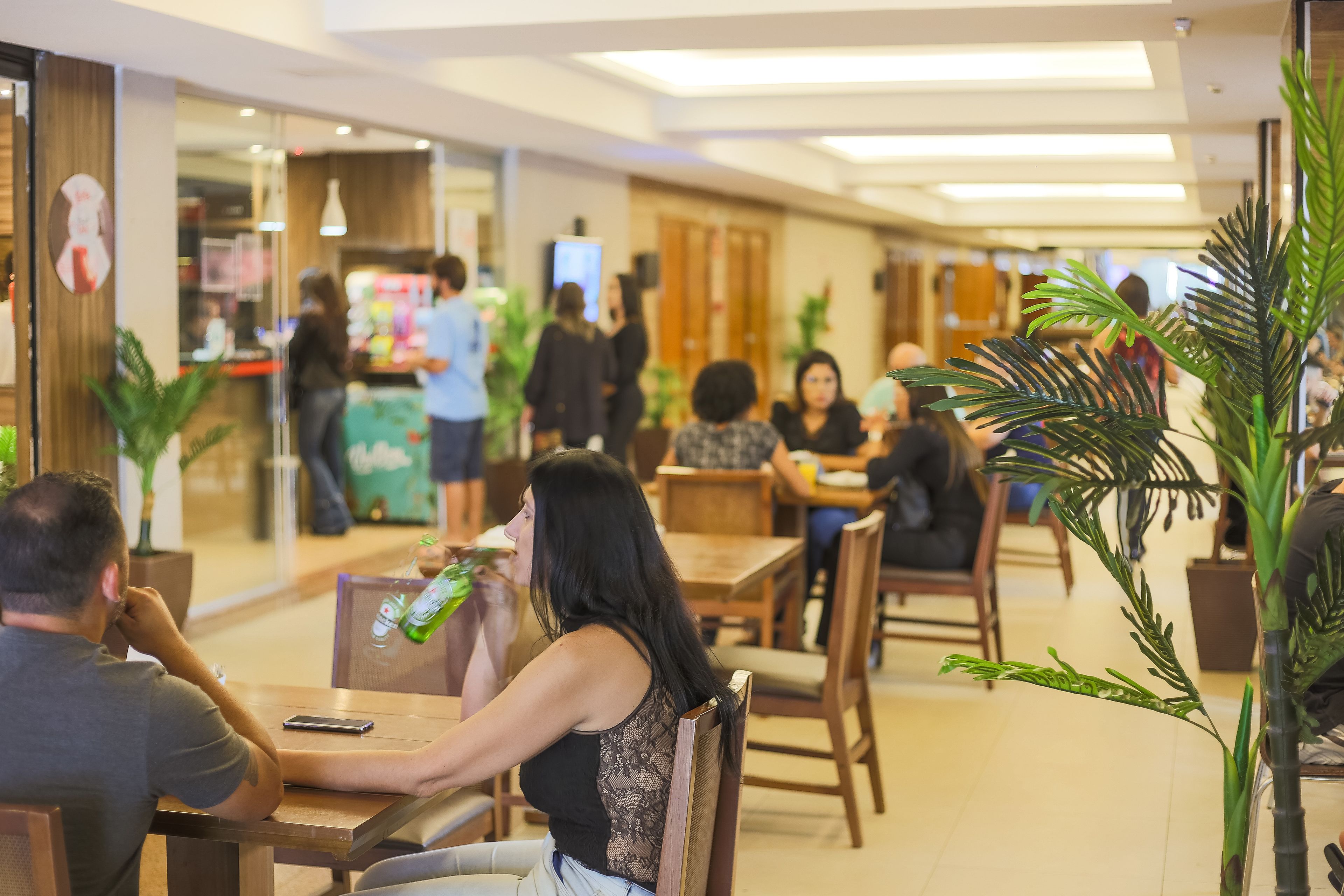 Um restaurante com mesas e cadeiras de madeira, plantas em vasos e um ambiente descontraído para refeições.