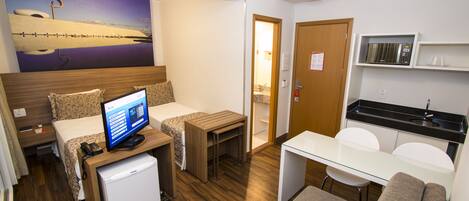 Habitación de hotel compacta con cama, escritorio, refrigerador pequeño, microondas y kitchenette.