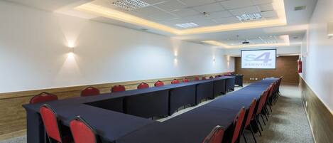 A conference room with a long table, red chairs, and a projection screen displaying "S4 EVENTOS".