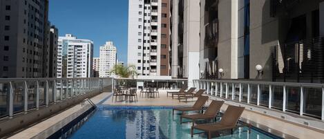 Una piscina al aire libre con sillas de descanso, rodeada de edificios altos.