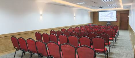 A conference room with rows of red chairs, a projector screen displaying "S4 EVENTOS", and a wooden accent wall.