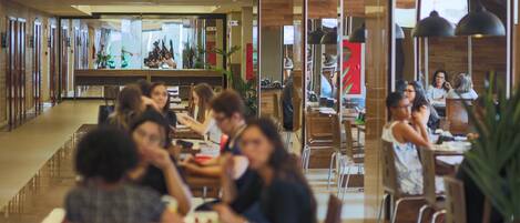 A modern dining area with multiple tables and chairs, a long counter, and a variety of plants.