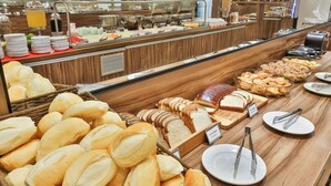 A buffet with various bread and pastries, including baguettes and sliced bread.