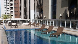 A rooftop pool with lounge chairs and a bar area, surrounded by modern buildings.