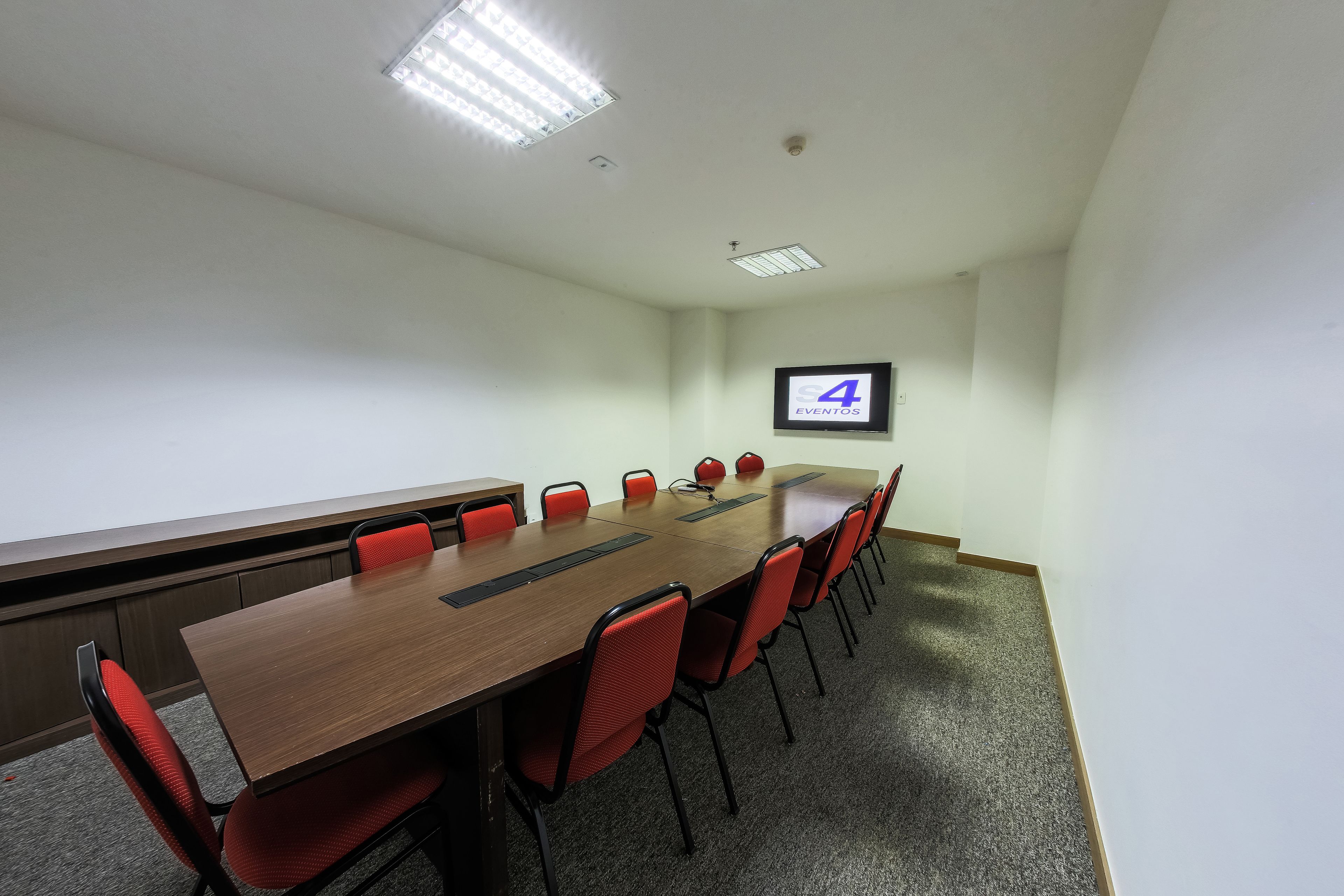 A conference room with a long table, red chairs, a projector screen, and a carpeted floor.