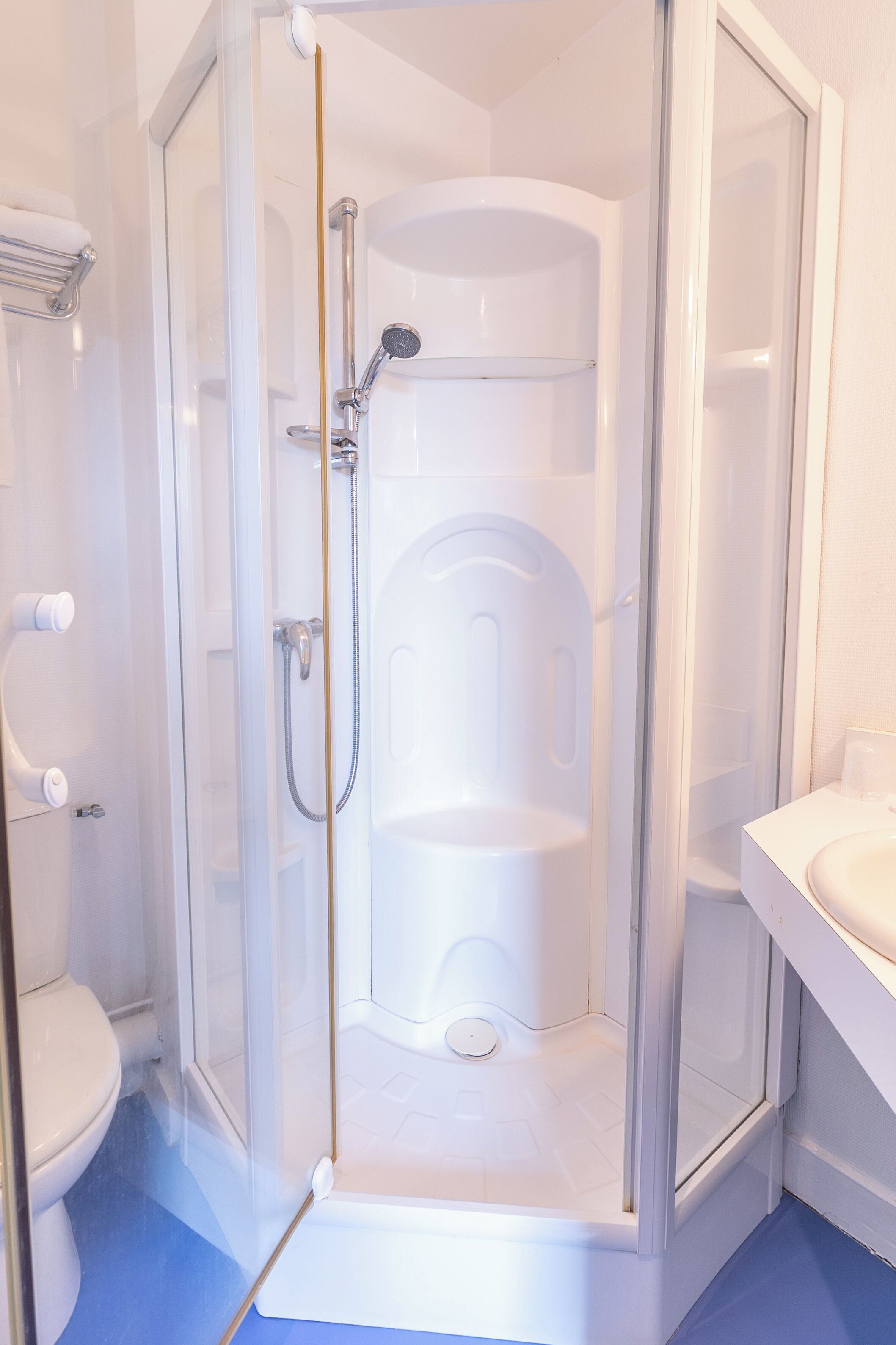 Un box de ducha con paredes de vidrio, una puerta blanca, un lavamanos blanco y un inodoro visible en la habitación contigua.