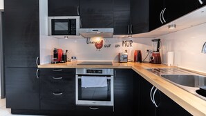 Una cocina moderna con gabinetes negros, un lavamanos de acero inoxidable, horno empotrado, microondas y cafetera.