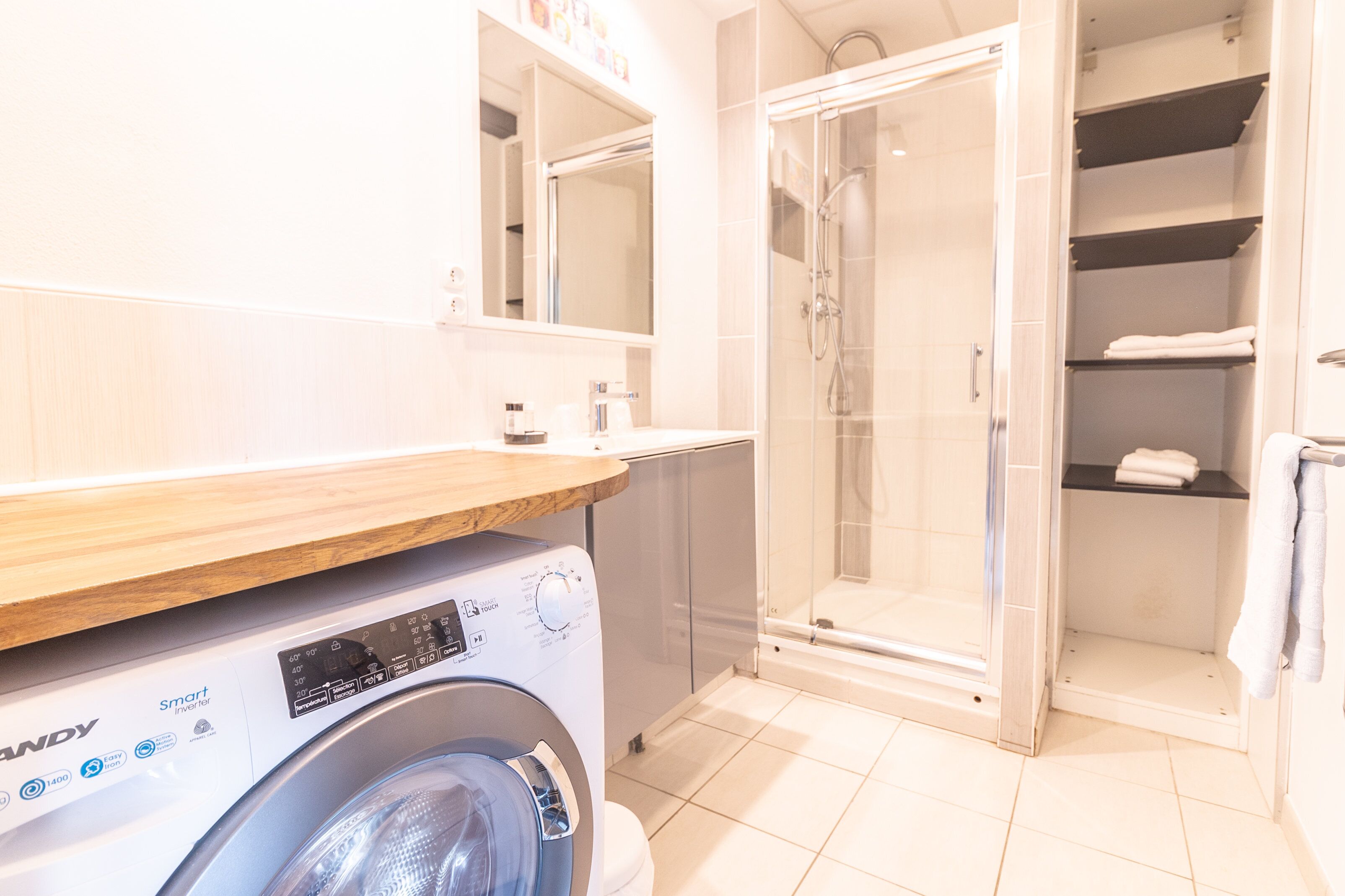 A modern bathroom with a washing machine, a glass-enclosed shower, and a built-in shelving unit.