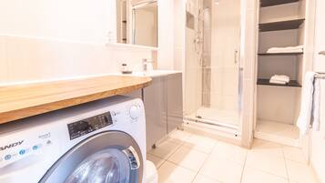 A modern bathroom with a washing machine, a glass-enclosed shower, and a built-in shelving unit.