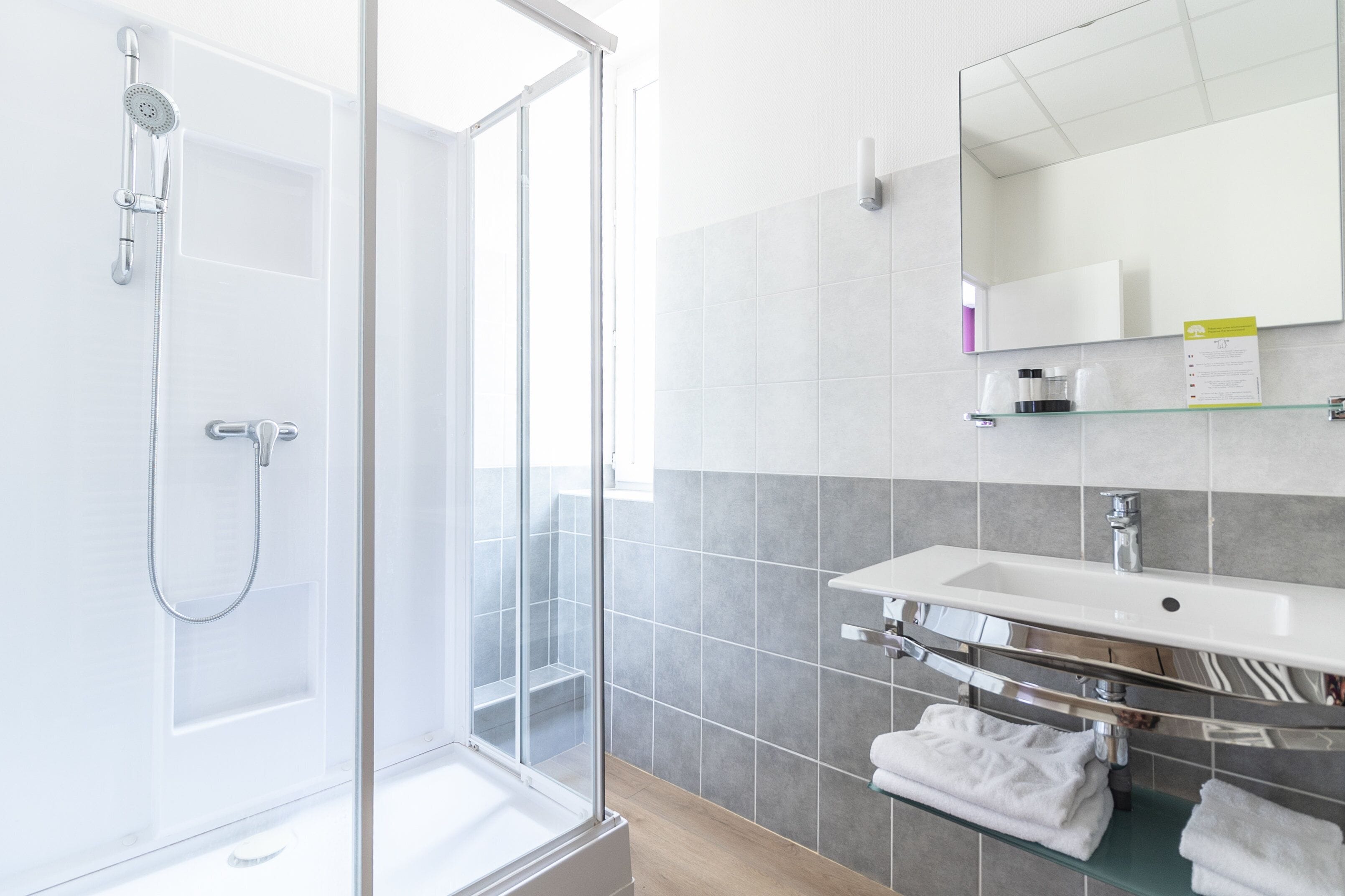 Ein modernes Badezimmer mit Duschkabine aus Glas, Waschbecken mit Spiegel darüber und Handtuchhalter.