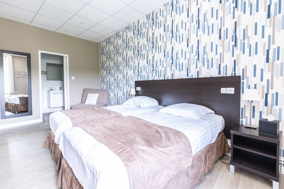 Een hotelkamer met een groot bed, nachtkastje, spiegel en een behang met patroon.