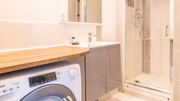 A modern bathroom with a washing machine, a glass shower enclosure, and a wooden countertop.