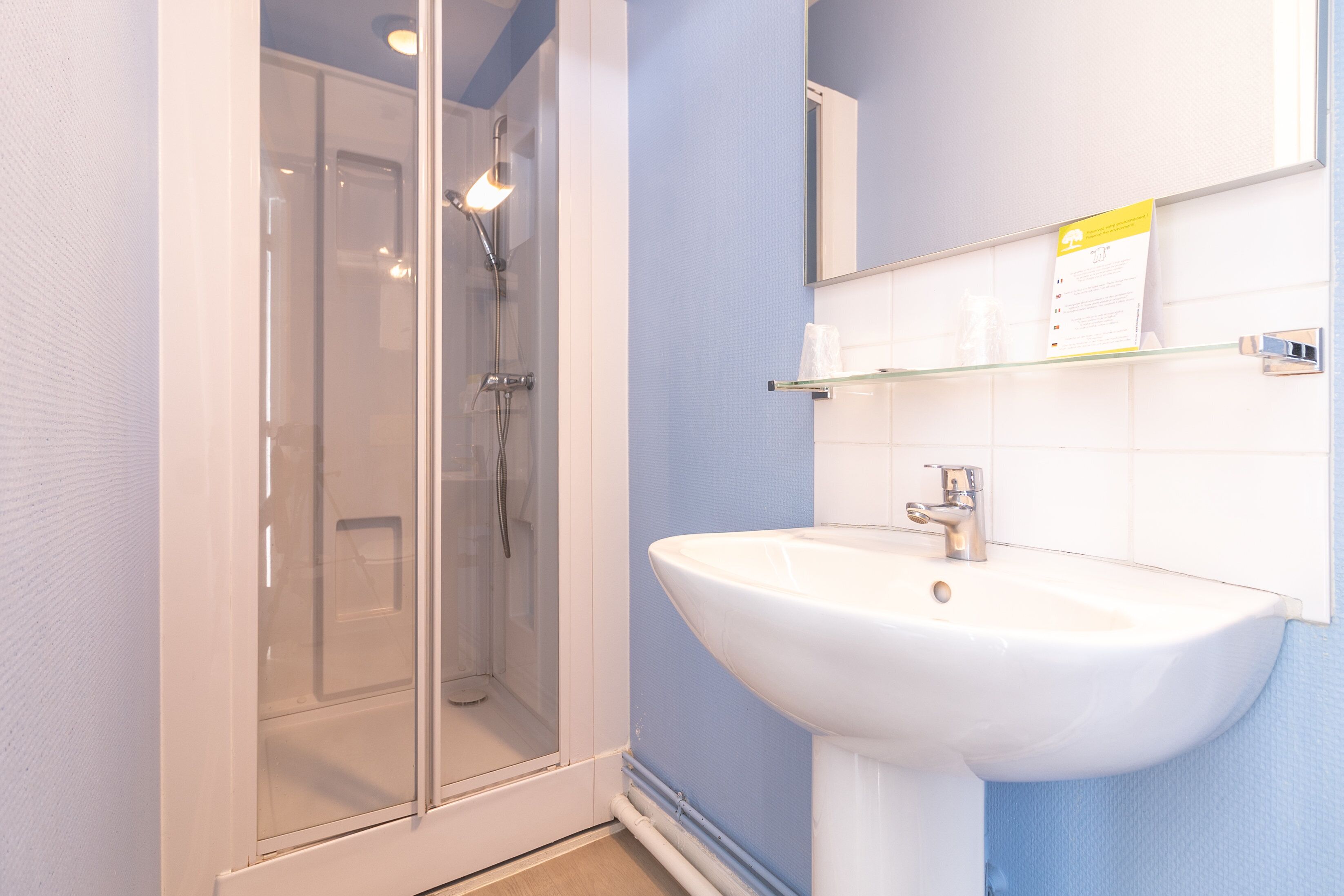 A bathroom with a glass shower enclosure, a white sink, and a mirror above the sink.