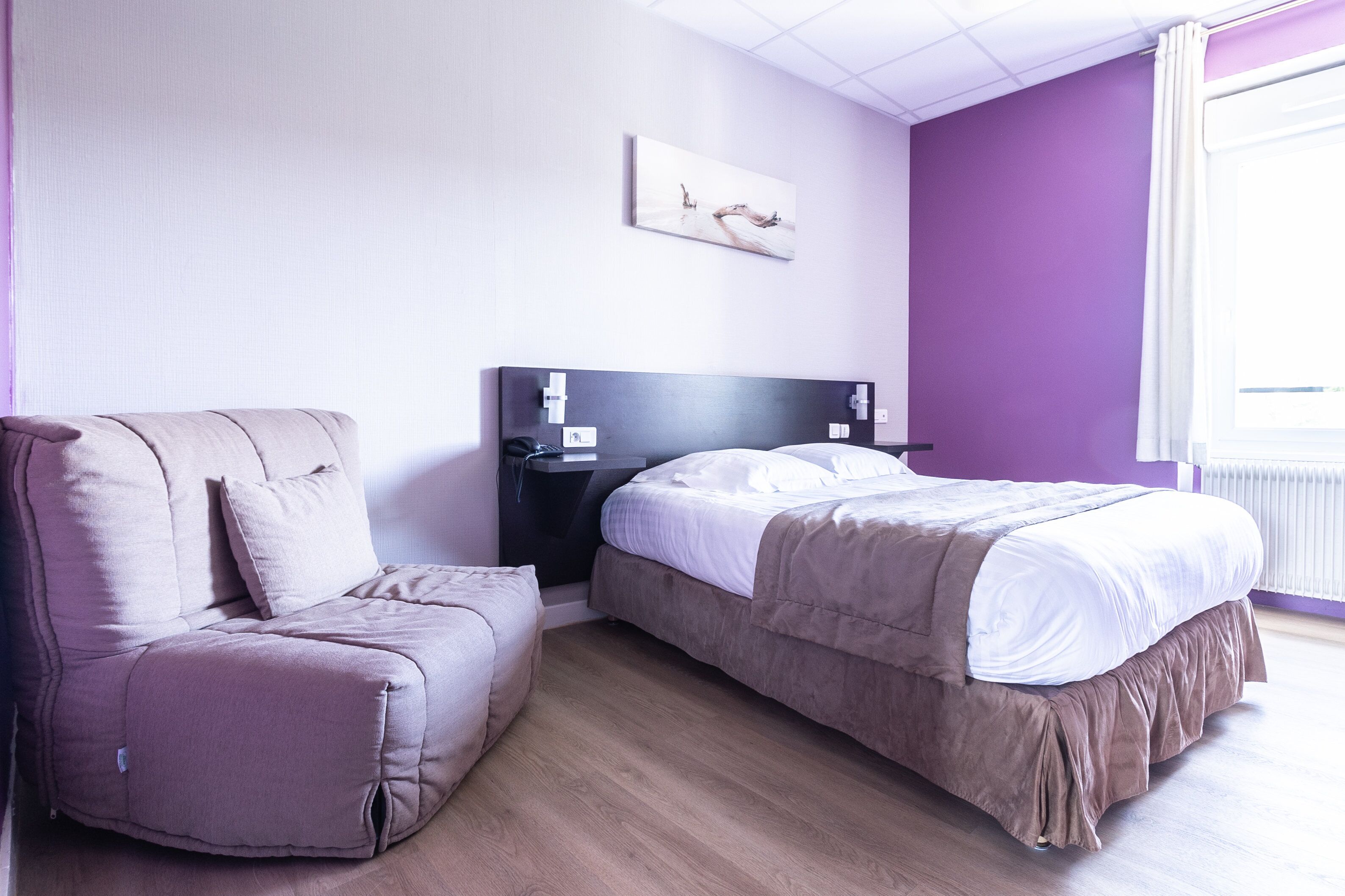 Een slaapkamer met een bed, een bank, een nachtkastje en een aan de muur hangend kunstwerk.