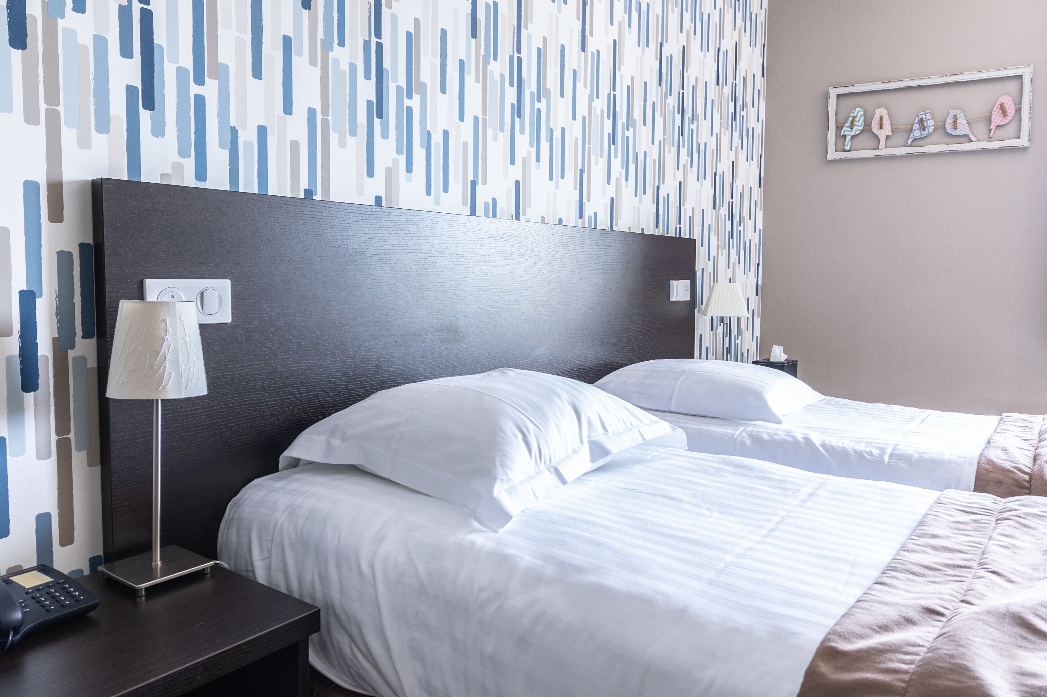 A hotel room with two beds, a nightstand, a lamp, and a wall with a geometric pattern.