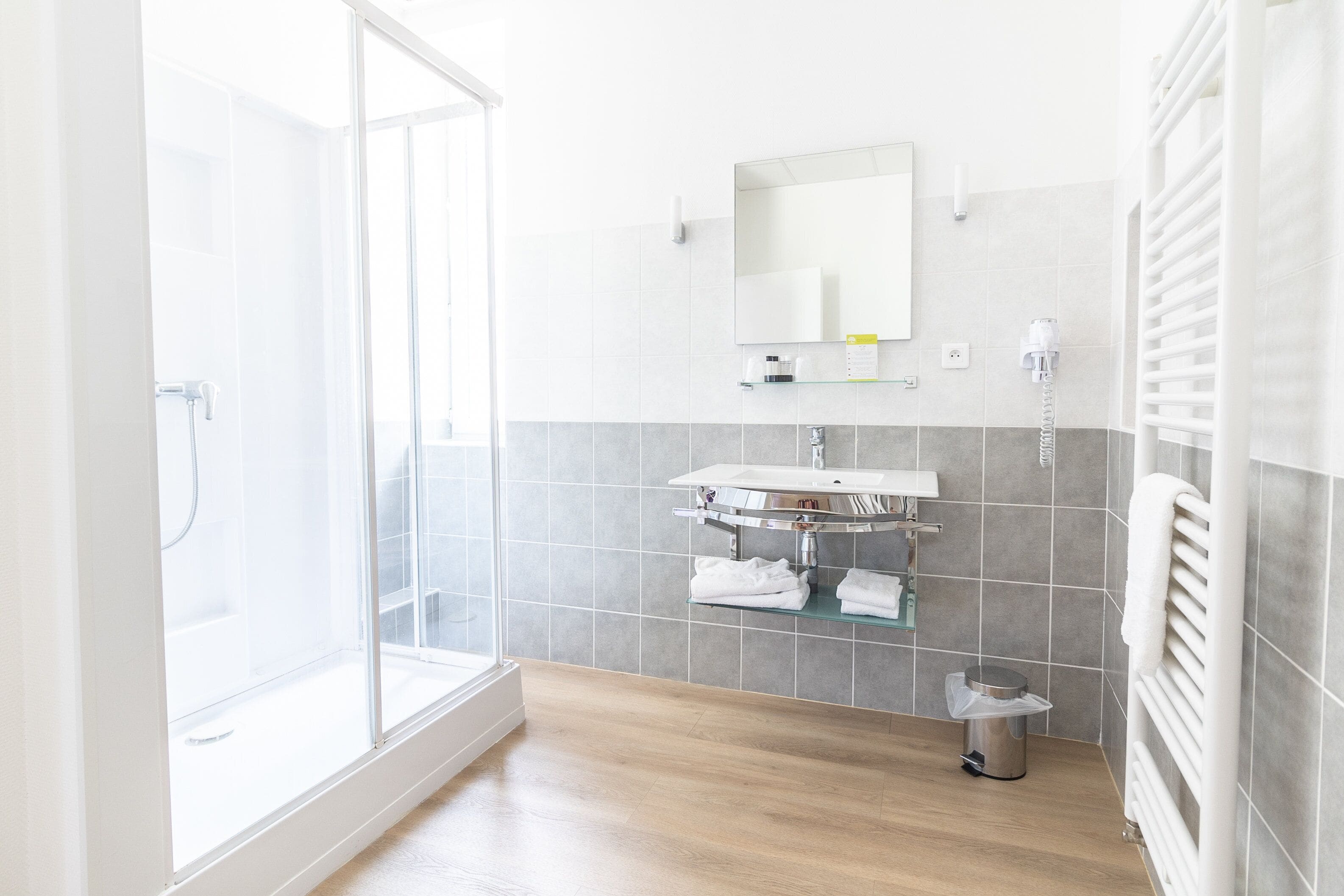 A modern bathroom with a glass shower enclosure, a white sink, and a towel rack.