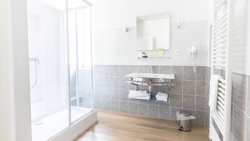 A modern bathroom with a glass shower enclosure, a white sink, and a towel rack.