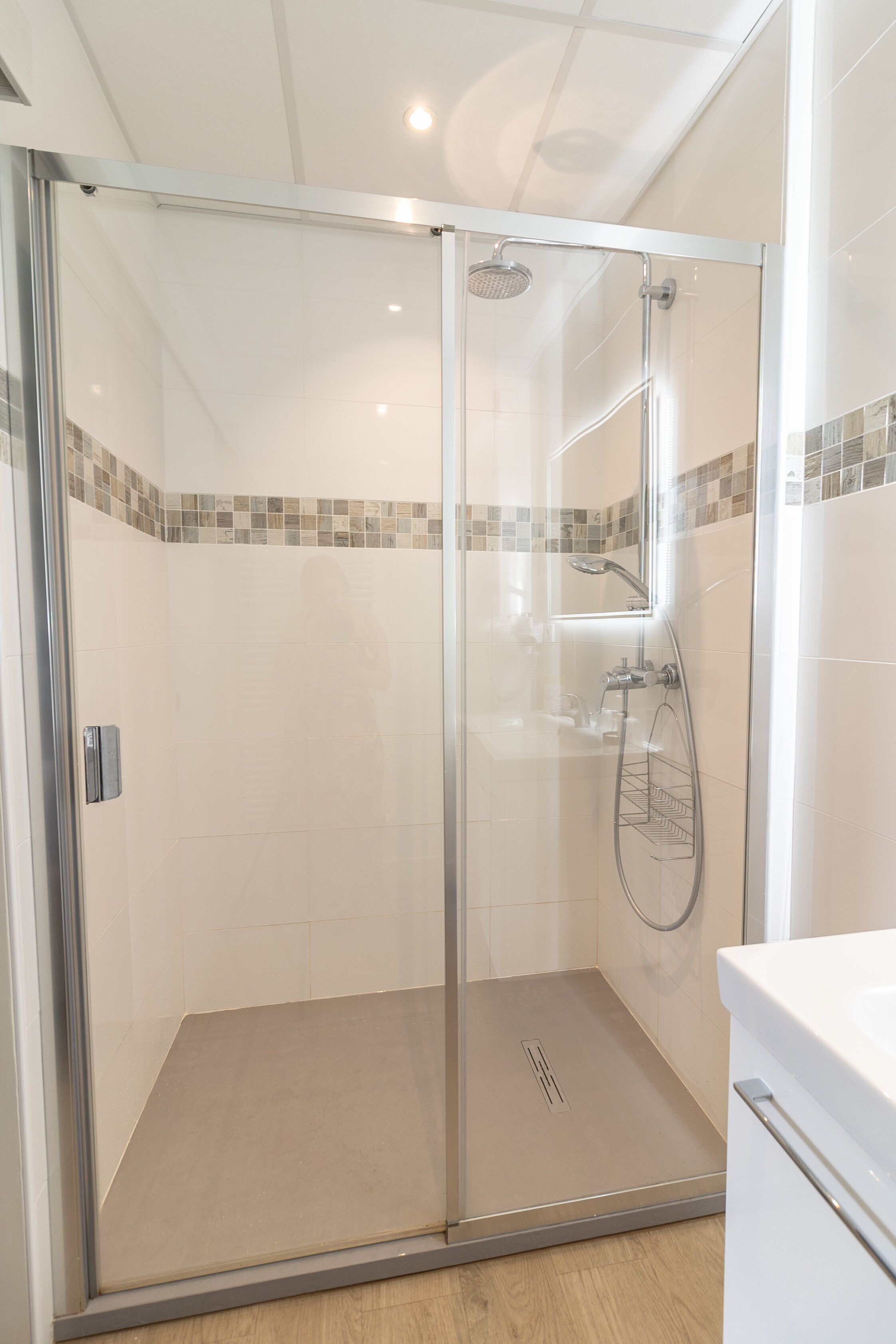 Um chuveiro com box de vidro, um chuveiro manual, uma porta de vidro e piso ladrilhado.