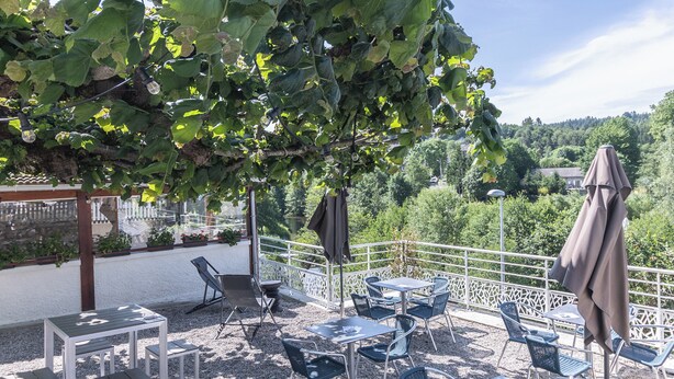Un patio al aire libre con mesas y sillas, rodeado de follaje y vistas a un lago.