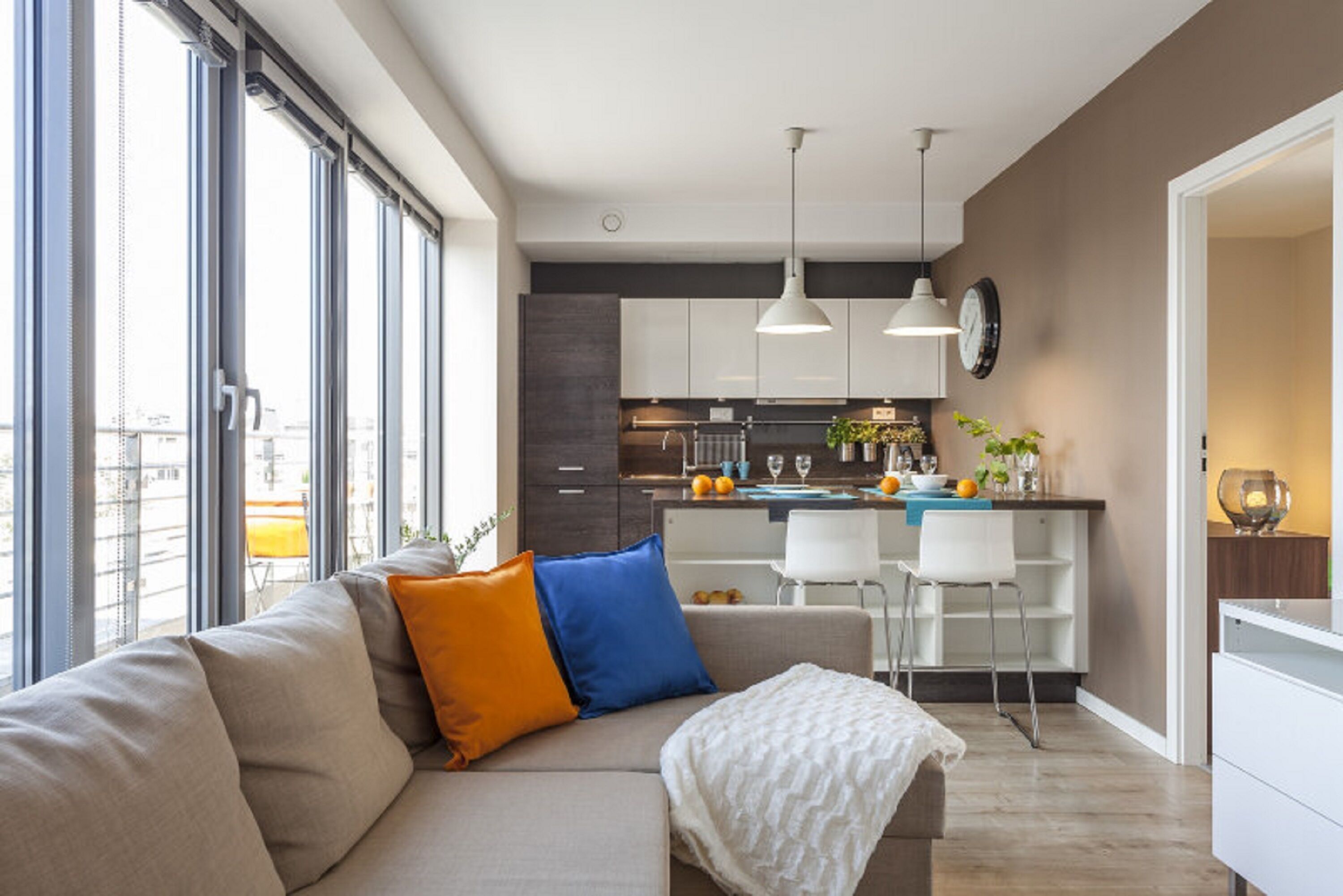 Una sala de estar moderna con un sofá, una mesa de centro y un comedor con sillas, y una cocina al fondo.