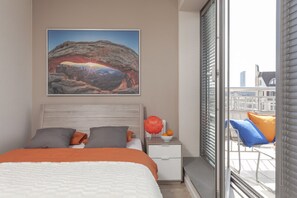 A bedroom with a bed, pillows, a nightstand, a window with blinds, and a city view. - Absynt Apartments Old Town Deluxe (Wroclaw)