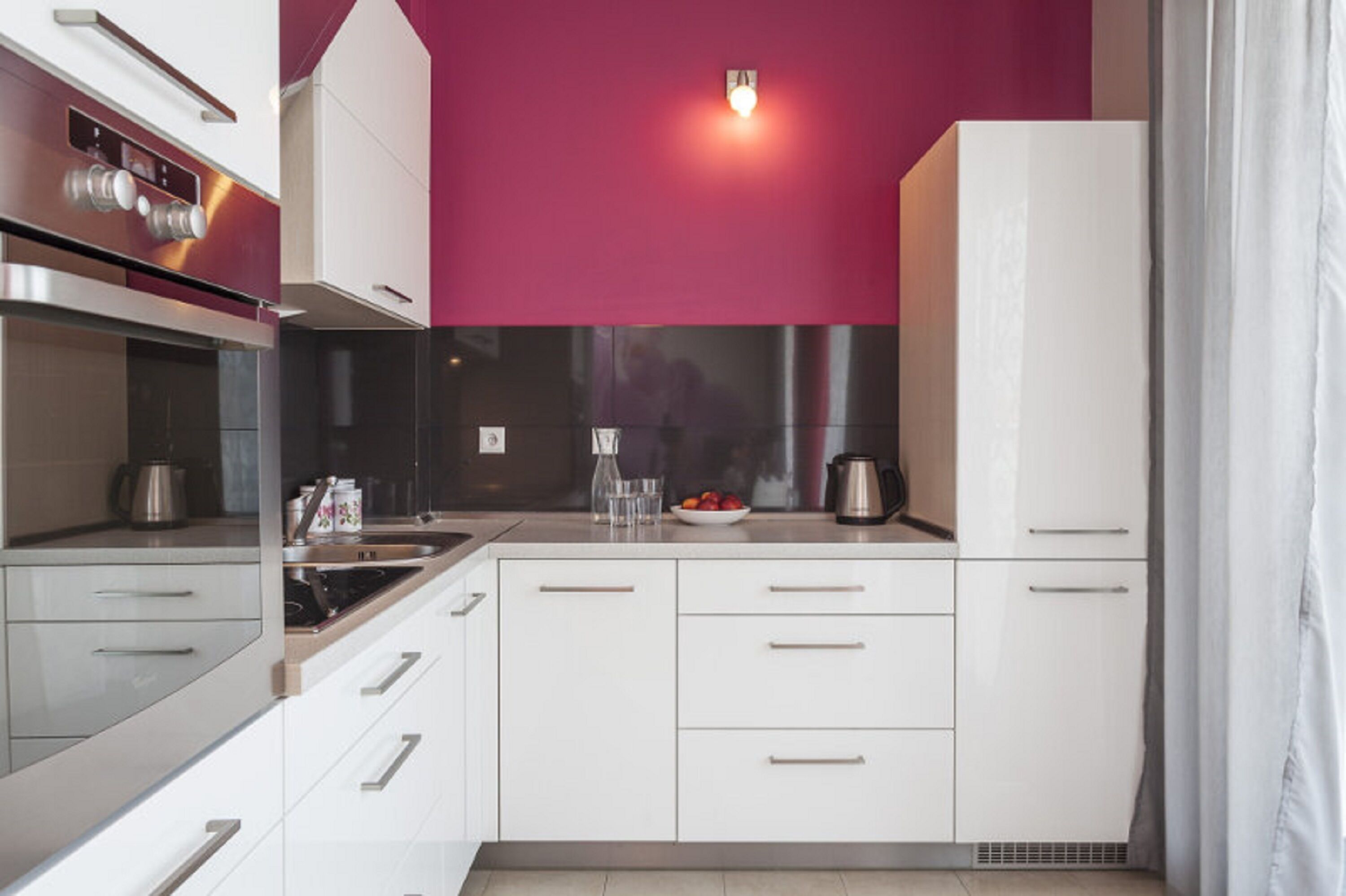 A modern kitchen with white cabinets, stainless steel appliances, and a red accent wall.