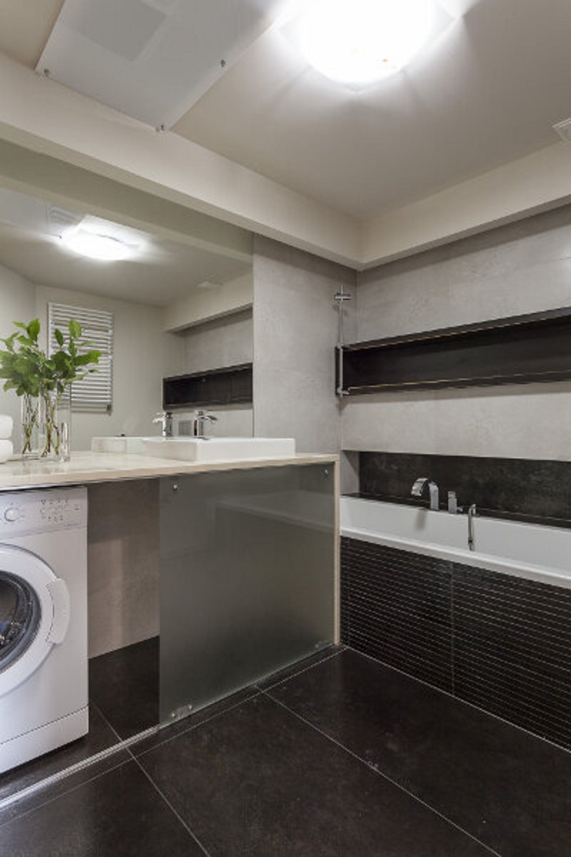 Une salle de bain moderne équipée d’un lave-linge intégré, d’un grand miroir, d’une baignoire et d’une douche.