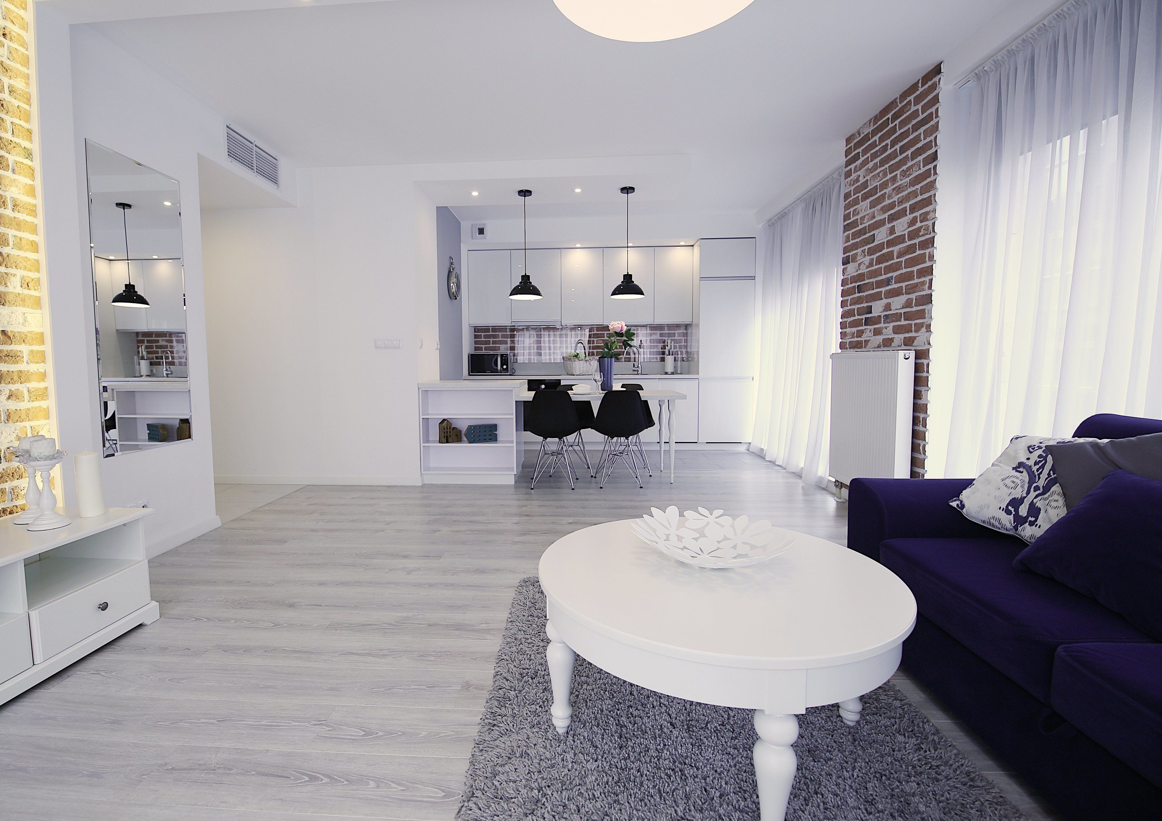 A modern living room with a white coffee table, a purple sofa, and a kitchen in the background.