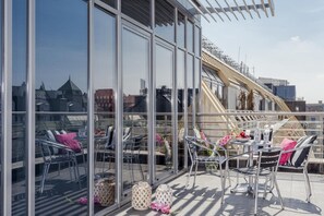 A rooftop terrace with glass walls, metal chairs, and a table set with flowers and a bowl of fruit. - Absynt Apartments Old Town Deluxe (Wroclaw)